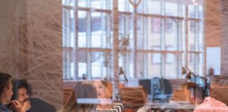 A startup team sits in a conference room with orange chairs and glass walls. They're all at the table talking.