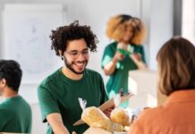 The Why and How of Hosting a Charity Event at Your Business A man in a green shirt and glasses smiles as a woman in an orange shirt hands him a box of donated goods.