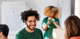A man in a green shirt and glasses smiles as a woman in an orange shirt hands him a box of donated goods.
