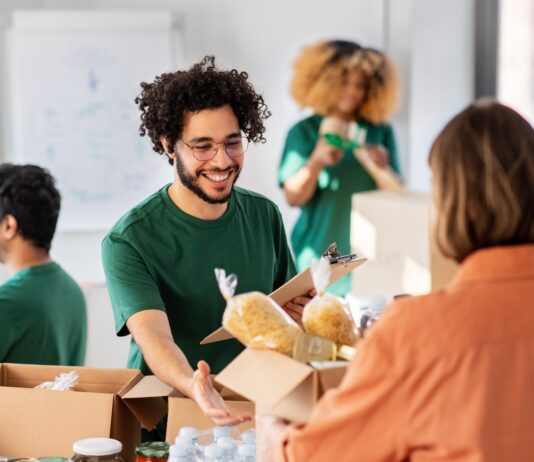 The Why and How of Hosting a Charity Event at Your Business A man in a green shirt and glasses smiles as a woman in an orange shirt hands him a box of donated goods.