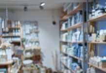 A well-organized retail store interior with wooden shelves displaying neatly arranged home goods, bath products, and decor items along a central aisle.