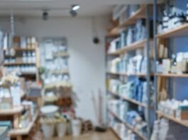 A well-organized retail store interior with wooden shelves displaying neatly arranged home goods, bath products, and decor items along a central aisle.