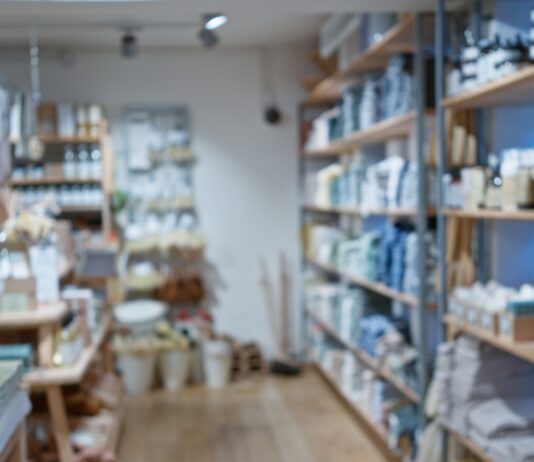 A well-organized retail store interior with wooden shelves displaying neatly arranged home goods, bath products, and decor items along a central aisle.