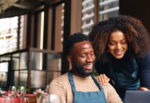 Details You Should Never Overlook When Running a Restaurant A man sitting behind a desk and a woman standing behind, both looking at a laptop inside a small restaurant.