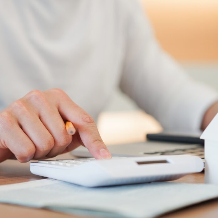 A person is sitting at a desk and is typing on a computer with one hand and typing on a calculator with the other.