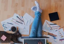 Reducing Stress When Working from Your Home Office A man is sitting on a hardwood floor with his legs crossed. There is a laptop sitting on his lap.