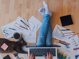 A man is sitting on a hardwood floor with his legs crossed. There is a laptop sitting on his lap.