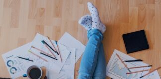 A man is sitting on a hardwood floor with his legs crossed. There is a laptop sitting on his lap.