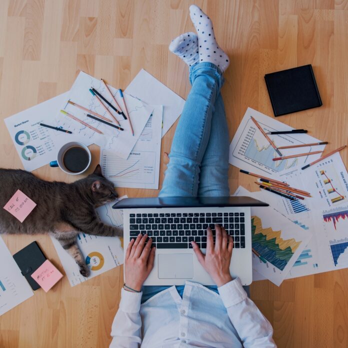 A man is sitting on a hardwood floor with his legs crossed. There is a laptop sitting on his lap. A man is sitting on a hardwood floor with his legs crossed. There is a laptop sitting on his lap.