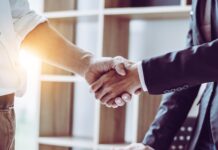 Managing Vendor Agreements in Small Businesses Two business professionals shake hands over a desk with documents, signaling an agreement or successful deal.