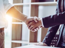 Managing Vendor Agreements in Small Businesses Two business professionals shake hands over a desk with documents, signaling an agreement or successful deal.