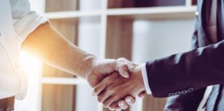Managing Vendor Agreements in Small Businesses Two business professionals shake hands over a desk with documents, signaling an agreement or successful deal.