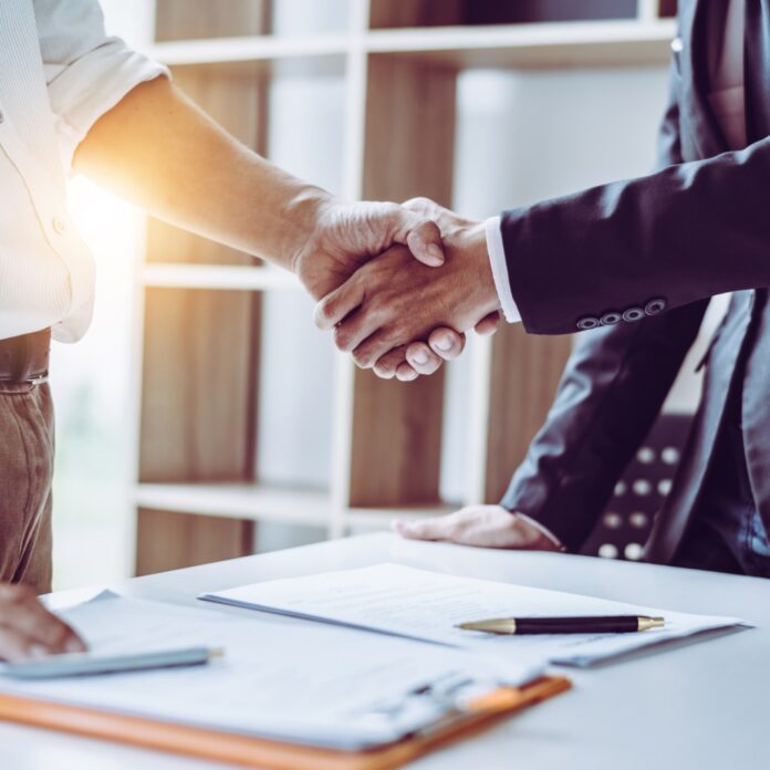Managing Vendor Agreements in Small Businesses Two business professionals shake hands over a desk with documents, signaling an agreement or successful deal.