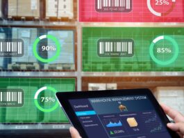 A worker holds a tablet showing warehouse data while shelves of goods display digital inventory tracking metrics.