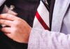 Screening Tools To Prevent Employee Substance Use at Work A close-up of a man’s chest wearing a black shirt and a striped tie, hiding a small flask under his grey suit jacket.