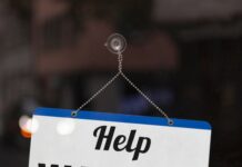 A small blue-and-white sign suction-cupped to a glass surface. The sign has text reading "Help Wanted" on it.