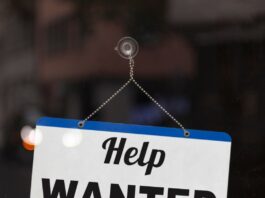 A small blue-and-white sign suction-cupped to a glass surface. The sign has text reading "Help Wanted" on it.