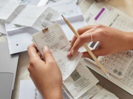 A business owner sits at the table with a bunch of receipts all over as they audit their business expenses.