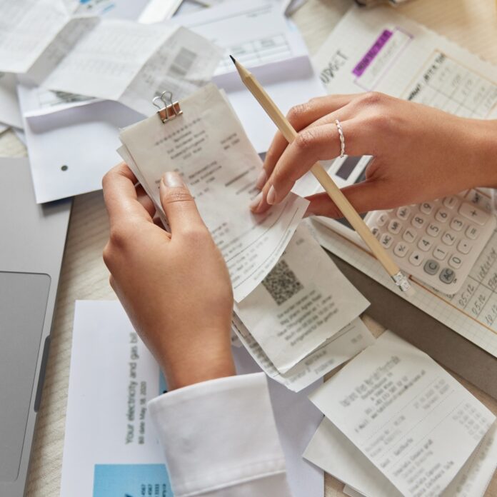 A business owner sits at the table with a bunch of receipts all over as they audit their business expenses. A business owner sits at the table with a bunch of receipts all over as they audit their business expenses.
