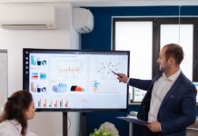 Why Wear a Suit While Presenting Ideas to Investors A man wearing a blue suit jacket, presenting on a large monitor in front of a room with people sitting on a desk.