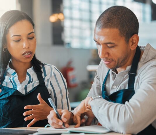 Two restaurant founders sit at a table and calculate the money needed to keep their business running.
