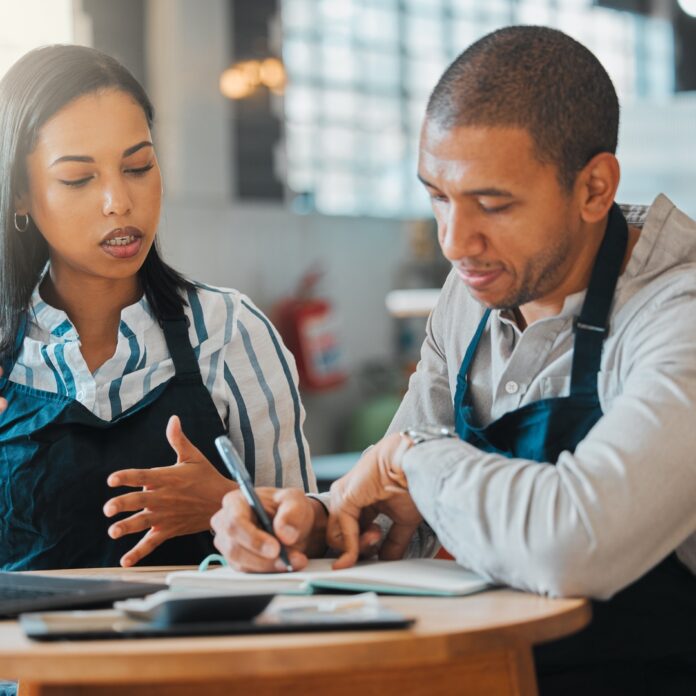 Two restaurant founders sit at a table and calculate the money needed to keep their business running. Two restaurant founders sit at a table and calculate the money needed to keep their business running.