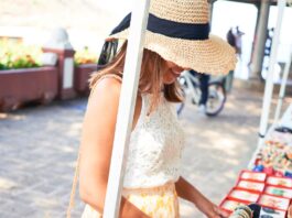 a smiling woman browsing colorful handmade souvenirs at an outdoor market kiosk on a sunny street with hanging displays.