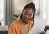 How Remote Work Can Complicate Your Business Taxes A remote business owner reviews paperwork while taking notes and working on a laptop from her bright home office.