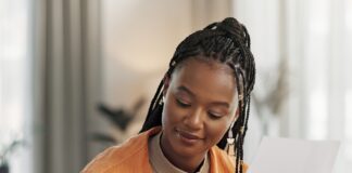 How Remote Work Can Complicate Your Business Taxes A remote business owner reviews paperwork while taking notes and working on a laptop from her bright home office.